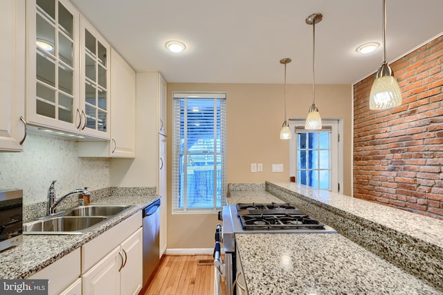 kitchen featuring backsplash, glass insert cabinets, appliances with stainless steel finishes, light wood-style floors, and a sink