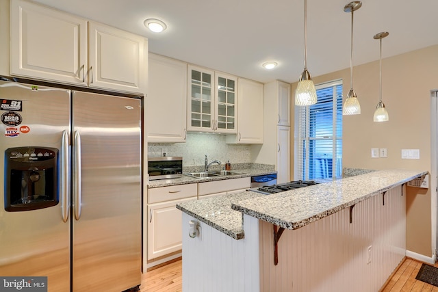 kitchen with a breakfast bar, a sink, light wood-style floors, appliances with stainless steel finishes, and a peninsula