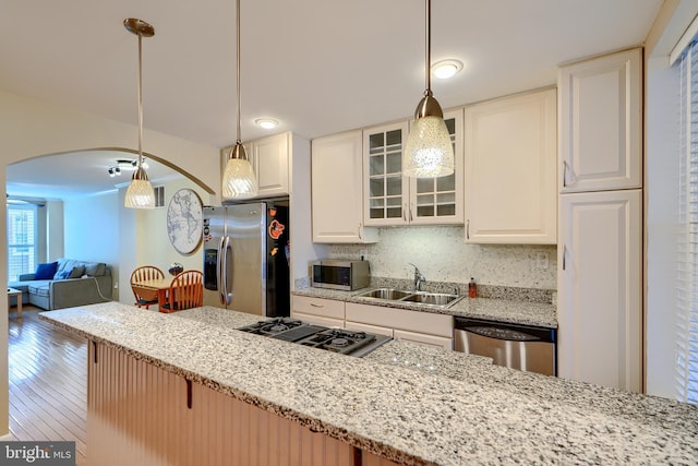 kitchen with arched walkways, a sink, stainless steel appliances, glass insert cabinets, and tasteful backsplash