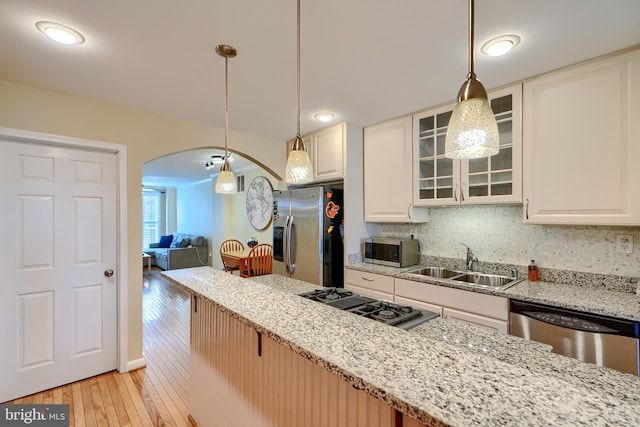 kitchen with light wood finished floors, light stone countertops, arched walkways, stainless steel appliances, and a sink