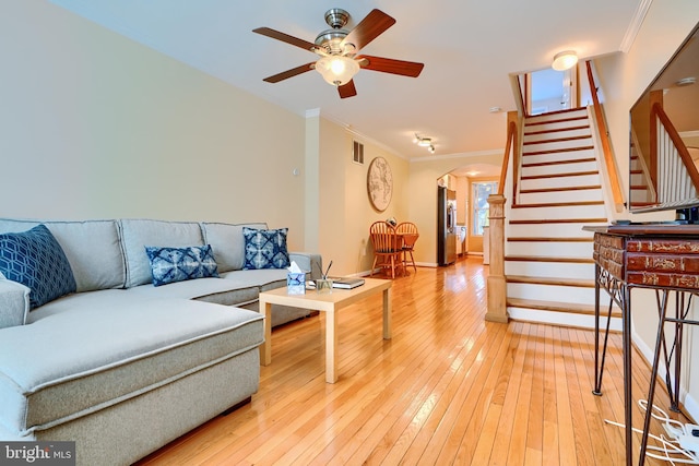 living room with arched walkways, light wood-style flooring, crown molding, and stairs