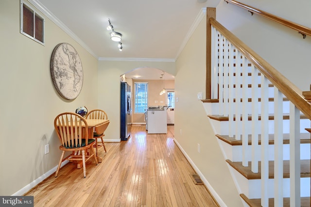 foyer entrance with visible vents, arched walkways, light wood-style floors, crown molding, and baseboards