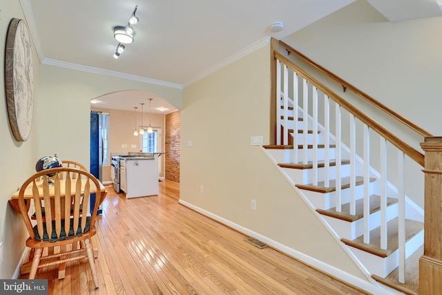 interior space with light wood finished floors, crown molding, baseboards, stairs, and arched walkways