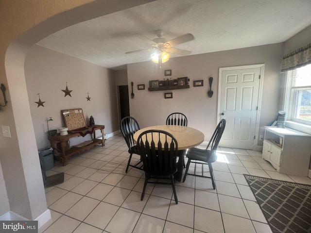 dining room with baseboards, arched walkways, light tile patterned flooring, and a ceiling fan