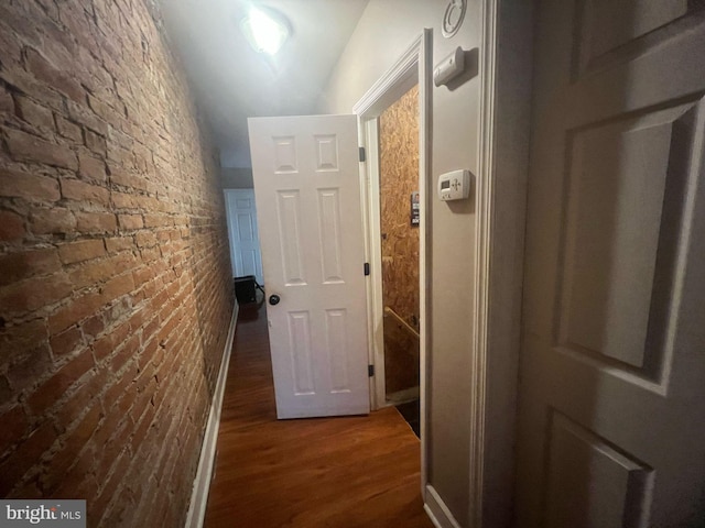 hall with wood finished floors and brick wall