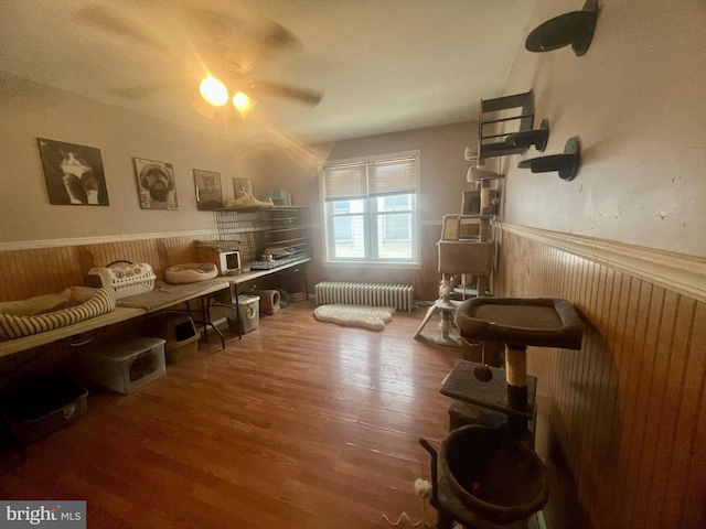 sitting room with wooden walls, radiator heating unit, wood finished floors, and wainscoting