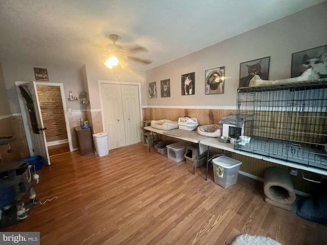 interior space featuring ceiling fan, a textured ceiling, wood finished floors, and wainscoting