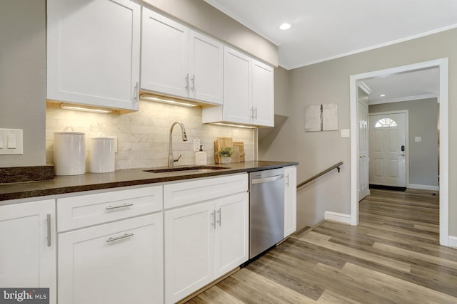 kitchen with dark countertops, ornamental molding, stainless steel dishwasher, white cabinets, and a sink