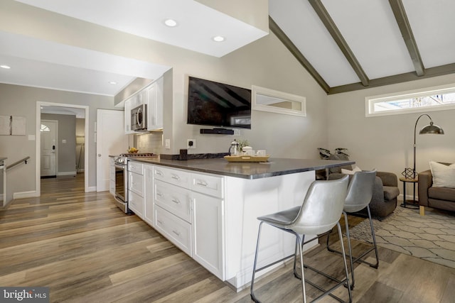 kitchen featuring stainless steel appliances, a kitchen bar, dark countertops, and white cabinets