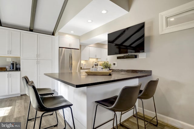 kitchen with dark countertops, freestanding refrigerator, light wood-style floors, a peninsula, and white cabinets