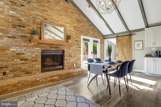 dining area with a barn door, a brick fireplace, beamed ceiling, and light wood-style flooring