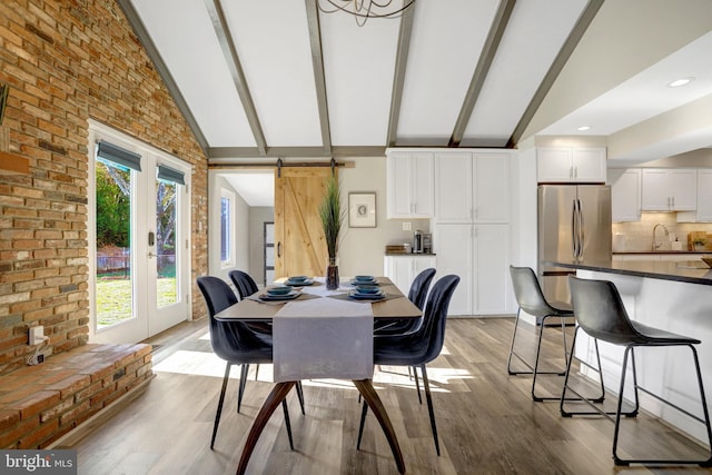 dining space with a barn door, lofted ceiling with beams, light wood-style floors, and brick wall