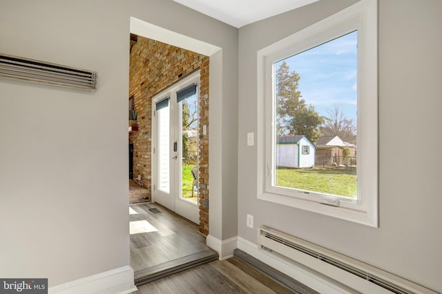 entryway with a baseboard radiator, baseboards, a brick fireplace, and wood finished floors