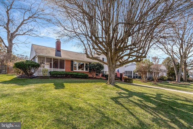 view of front facade featuring brick siding, a chimney, a front lawn, and a sunroom