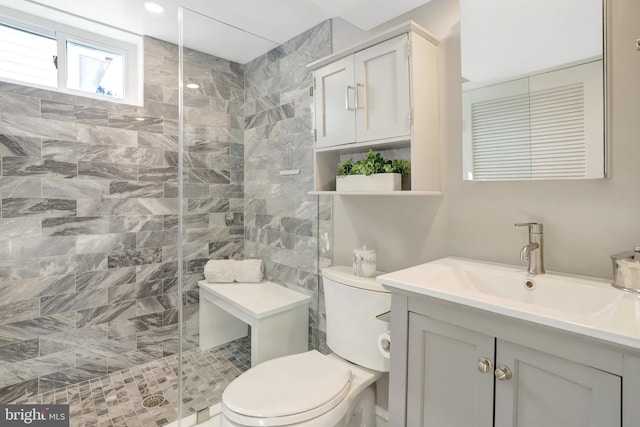 bathroom with a tile shower, toilet, and vanity