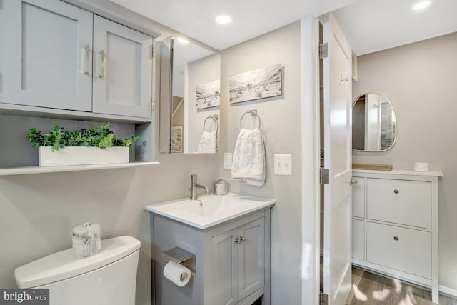 bathroom featuring wood finished floors, two vanities, recessed lighting, a sink, and toilet