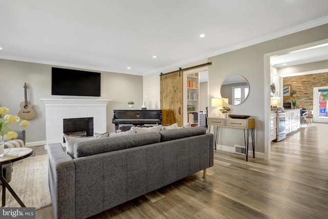 living room with a barn door, a brick fireplace, wood finished floors, and ornamental molding