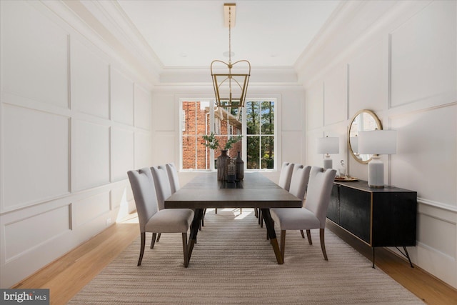 dining space featuring a notable chandelier, light wood-style floors, ornamental molding, and a decorative wall