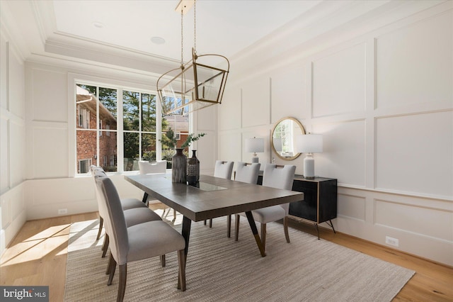 dining space with light wood-type flooring, a notable chandelier, crown molding, and a decorative wall