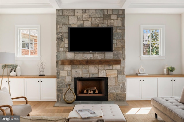 living room with a stone fireplace, beamed ceiling, and light wood finished floors