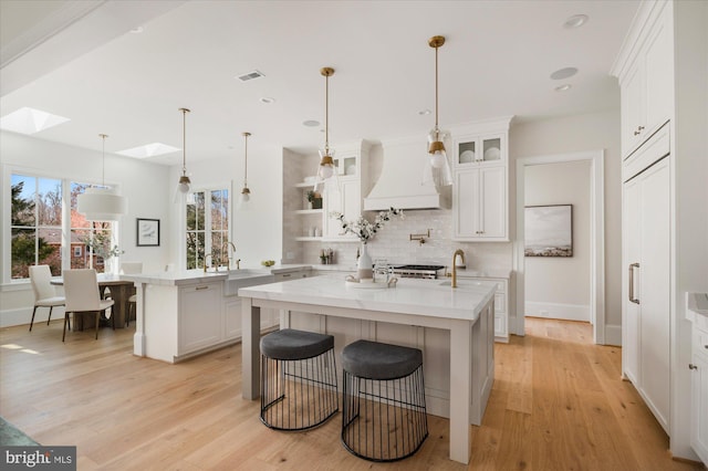 kitchen featuring an island with sink, light wood-style floors, a peninsula, decorative backsplash, and custom exhaust hood