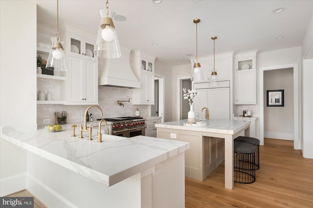 kitchen featuring premium range hood, light wood-style flooring, open shelves, premium appliances, and a peninsula