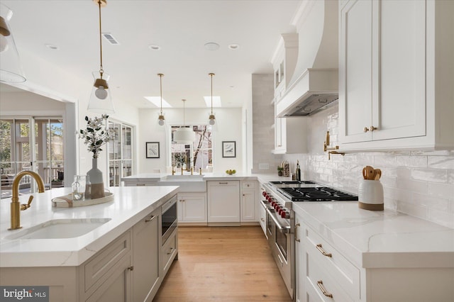 kitchen featuring premium range hood, a peninsula, a sink, stainless steel appliances, and tasteful backsplash