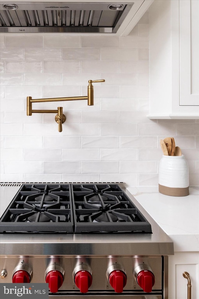 interior details with gas stove, backsplash, and white cabinetry