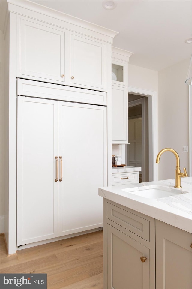 kitchen with light stone countertops, a sink, glass insert cabinets, light wood-style floors, and white cabinetry