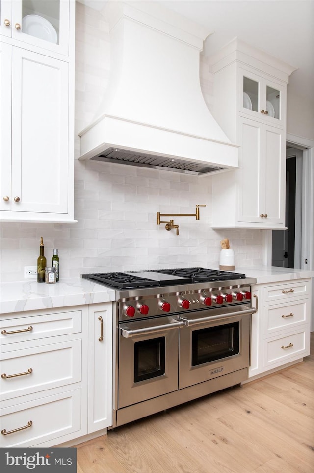 kitchen with tasteful backsplash, light wood finished floors, double oven range, custom exhaust hood, and white cabinets