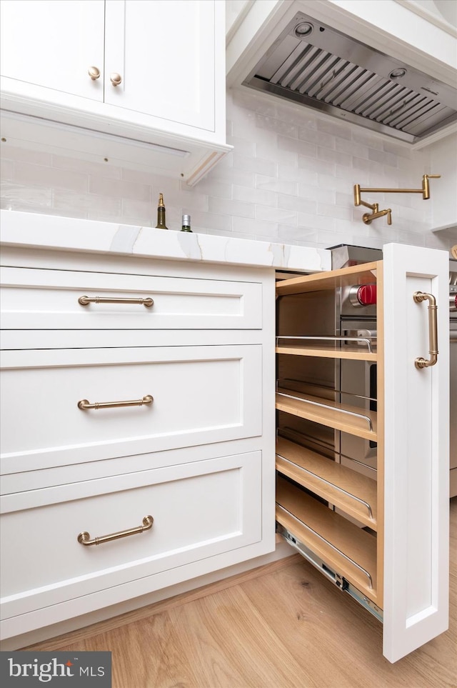 interior details featuring decorative backsplash, white cabinets, ventilation hood, and light countertops