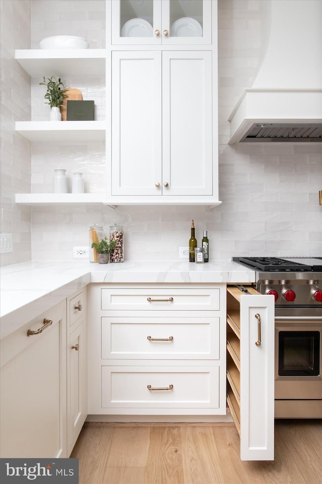 kitchen with custom exhaust hood, white cabinets, and high end stainless steel range oven