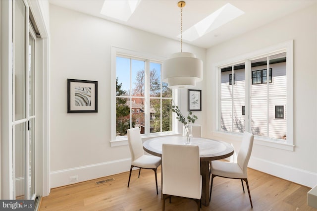 dining space with a skylight, plenty of natural light, light wood-style flooring, and visible vents