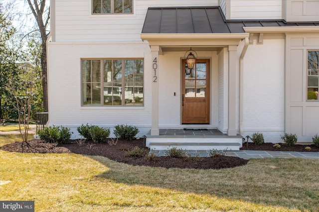 entrance to property featuring a standing seam roof, a lawn, brick siding, and metal roof