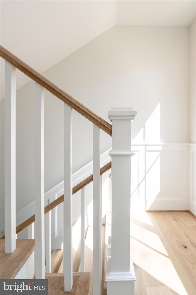 staircase featuring wainscoting, wood finished floors, and vaulted ceiling