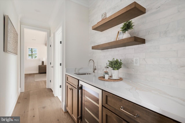 bar with beverage cooler, a sink, crown molding, light wood-type flooring, and backsplash