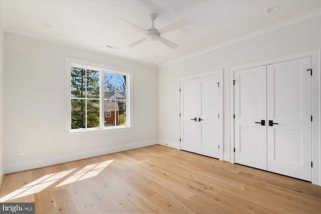 unfurnished bedroom with crown molding, visible vents, multiple closets, and light wood-type flooring