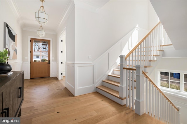 entryway featuring a wainscoted wall, stairs, light wood-type flooring, and ornamental molding