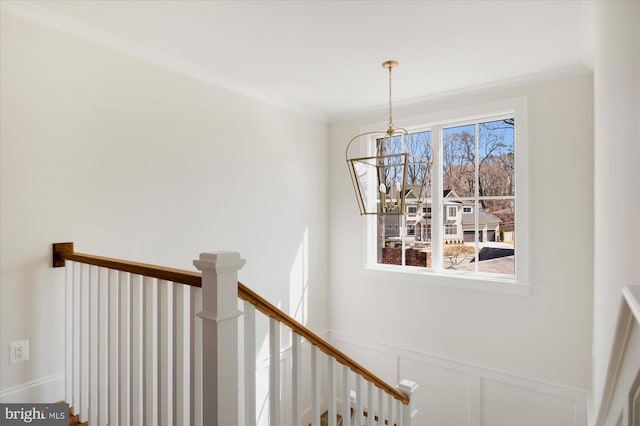 stairway featuring ornamental molding, a chandelier, wainscoting, and a decorative wall