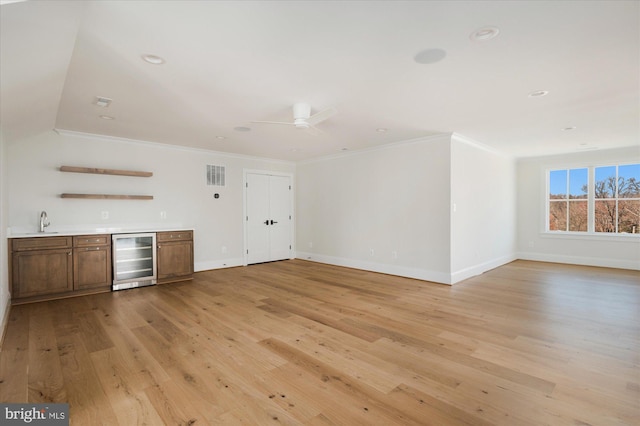 unfurnished living room featuring light wood finished floors, visible vents, beverage cooler, wet bar, and a sink