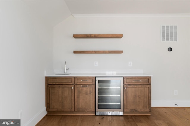 bar with visible vents, beverage cooler, wet bar, wood finished floors, and a sink