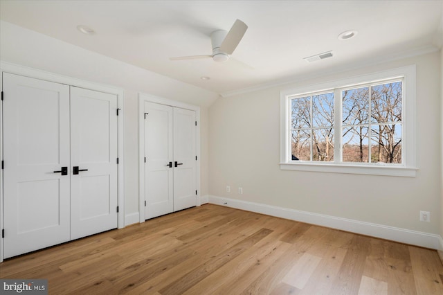 unfurnished bedroom featuring visible vents, light wood-style flooring, two closets, and baseboards