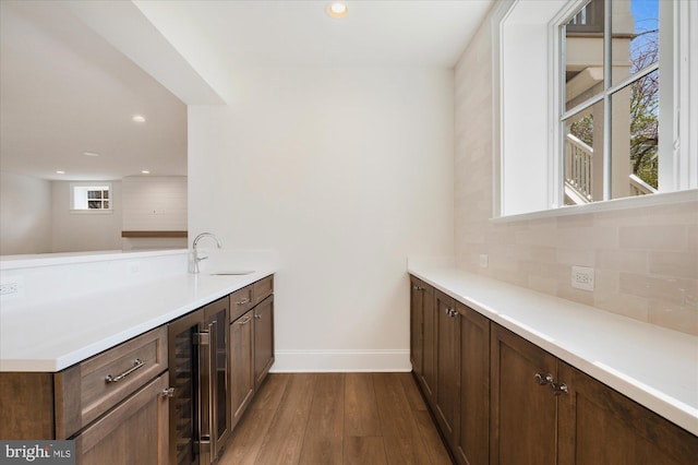 kitchen with wine cooler, dark wood finished floors, light countertops, a peninsula, and a sink