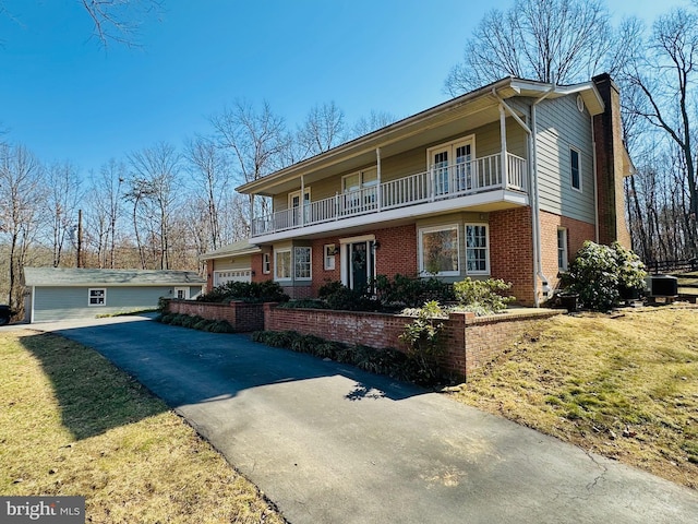 front of property with driveway, a balcony, a garage, brick siding, and a chimney