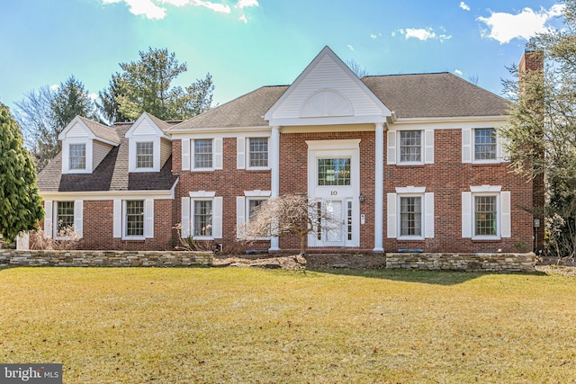 view of front of house with brick siding, roof with shingles, and a front yard