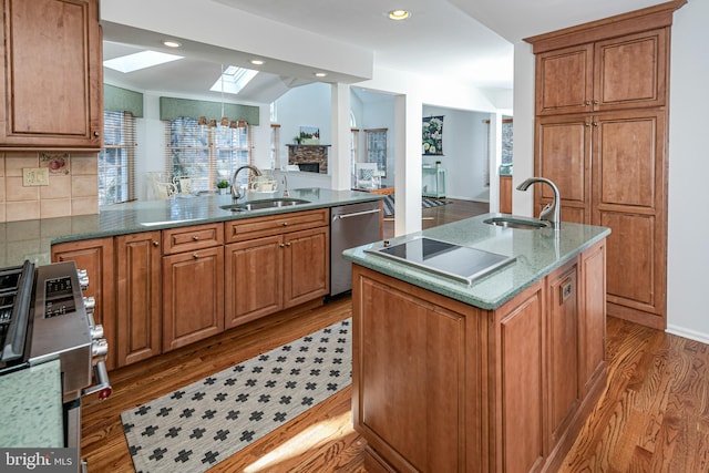 kitchen featuring brown cabinetry, a skylight, stainless steel appliances, a sink, and light wood-style floors