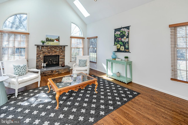 living area with baseboards, a fireplace, a skylight, wood finished floors, and high vaulted ceiling