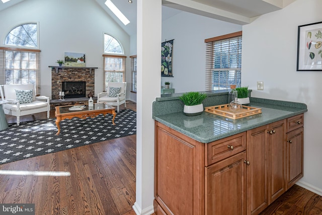 kitchen with a stone fireplace, dark wood-type flooring, a skylight, and brown cabinetry