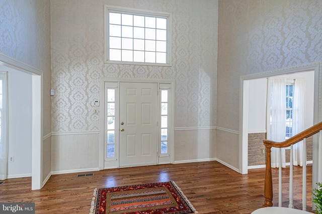 entryway featuring wallpapered walls, a high ceiling, wood finished floors, and a wainscoted wall