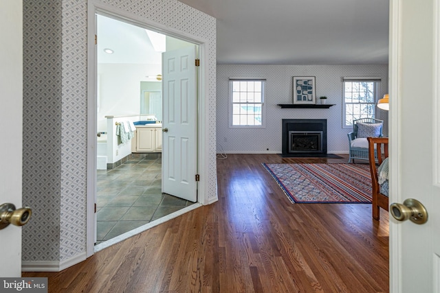 interior space featuring dark wood finished floors, a fireplace with flush hearth, wallpapered walls, and baseboards